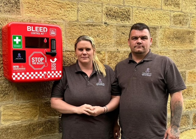 Micala and Lee Trussler, founders of Holly's Hope, standing beside a bleed control kit they have installed
